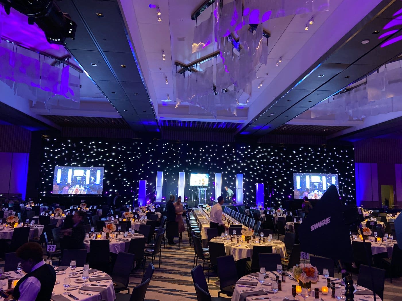 A ballroom gala with LED screens and a star cloth behind the stage