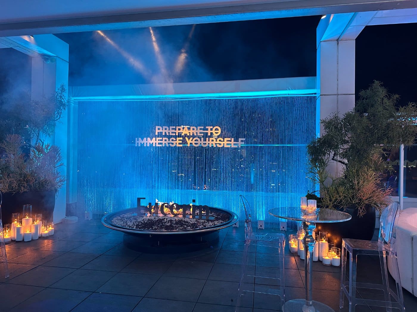 A brand activation lit in blue, with fire bowls and planting